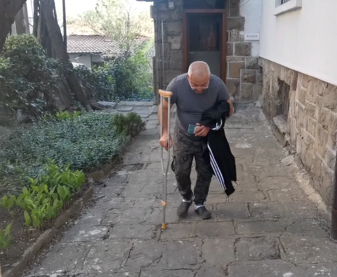 Светльо е в двора на клиниката, върви с патерица, скован от болка в кръста и крака от възпален нерв (ишиас).