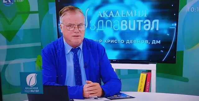 Снимка на Д-р Деянов, седнал на стол на водещия в предаването  Академия Здравитал по телевизия Евроком, в син костюм и вратовръзка.
